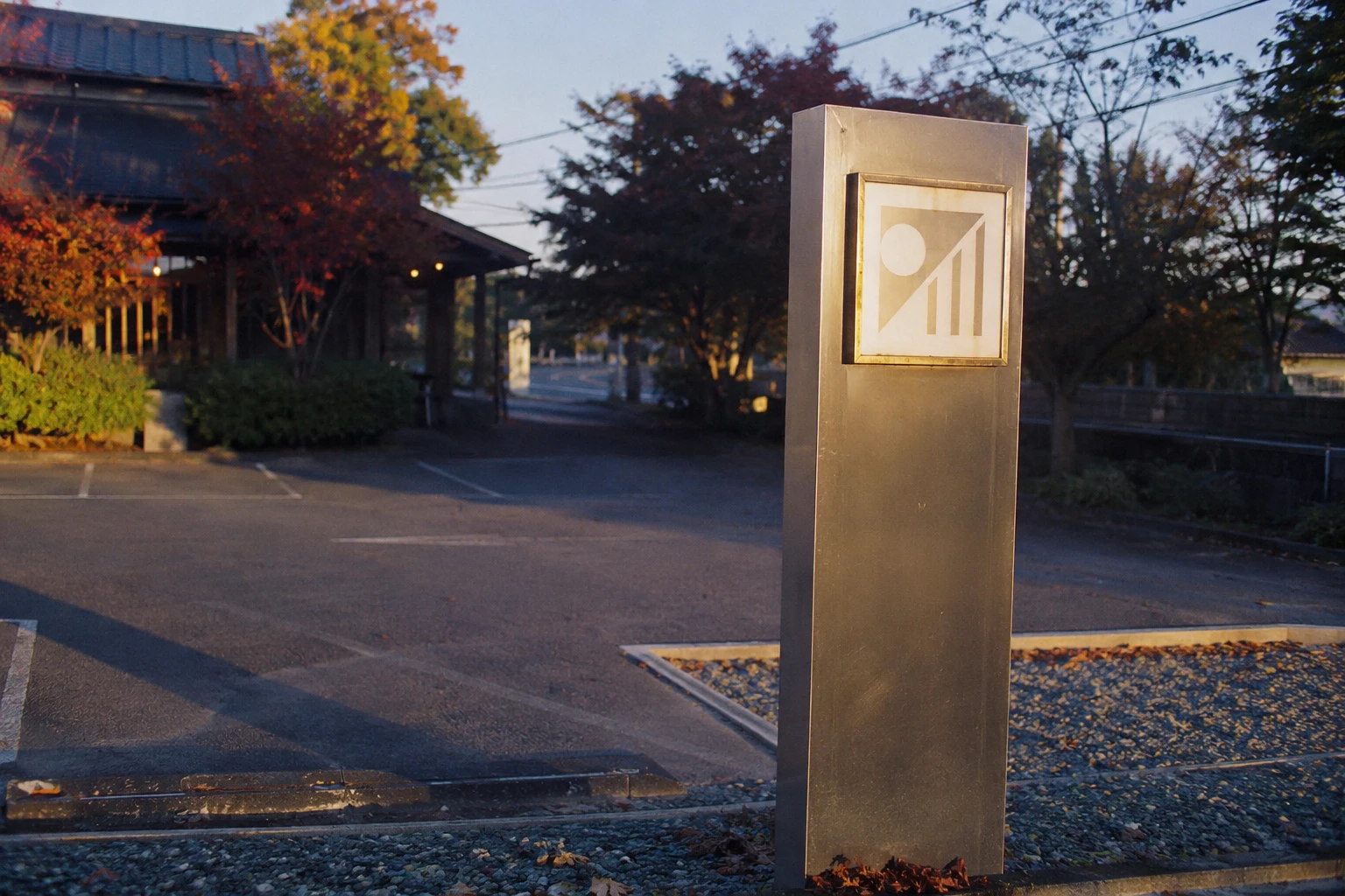 Freistehender Pylon aus gebürstetem Stahl mit beleuchtetem Logo-Element am Parkplatz-Eingang